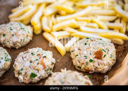 Macro closeup of frozen french chip fries, raw fish crab cakes on baking tray parchment paper for oven before cooking as traditional seafood meal Stock Photo