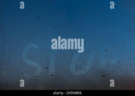 the word stop written on night wet window glass close-up with blurred background Stock Photo