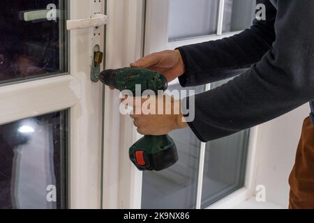 Handsome man using a screwdriver to install a window handle and looking at the camera. Making a house cozy and warm Stock Photo