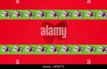 red background with green ribbons on which there are packages, red bow in the middle of the background, creative holiday concept Stock Photo