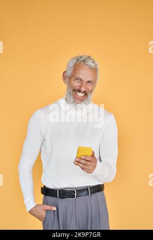 Happy old senior businessman using smartphone isolated on yellow. Vertical Stock Photo