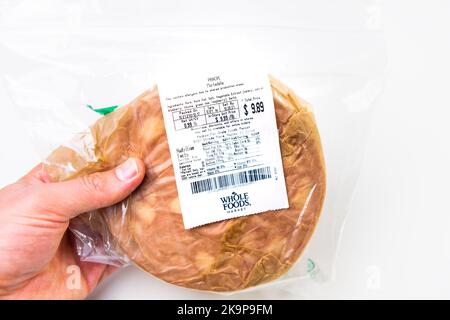 Naples, USA - October 21, 2021: Hand holding thin slices of pork cured Italian mortadella sausage bologna by Whole Foods market grocery store Stock Photo