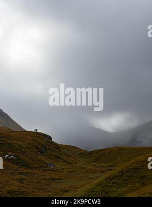 Two walkers in Glencoe pointing towards clearance in thick cloud, Glencoe, Scotland, UK Stock Photo