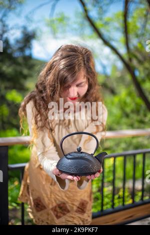 Young woman offering Japanese green tea from traditional teapot in modern luxury outdoor spring garden in backyard porch of zen home house Stock Photo