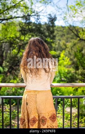 Young woman back standing by wooden fence railing in modern luxury outdoor spring garden in backyard porch on balcony terrace Stock Photo