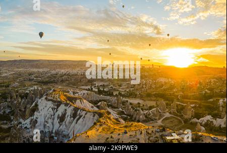 Summertime adventure. Rising sun illuminating beautiful sky full of hot-air balloons flying over the town of Cappadocia, Turkey. High quality photo Stock Photo