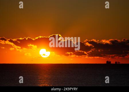 Dawn sun go behind cloud over sea horizon during dawn. Sunbeams, sun rays. Dawn sunrise dawning on sea. Black silhouettes of sea and clouds. Sky sea landscape. Seascape Fast moving clouds Stock Photo