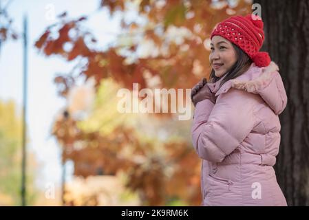 Asia woman feel cold in the park wearing winter accessories, pink sweater, gloves and crochet hats. Stock Photo