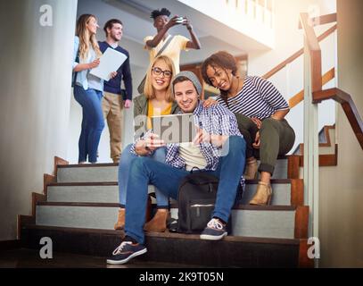 Catching up with some quick connections. a group of university students using a digital tablet on the staircase at campus. Stock Photo
