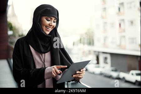 Putting her idea into action. an attractive young businesswoman dressed in Islamic traditional clothing using a tablet while standing on her office Stock Photo