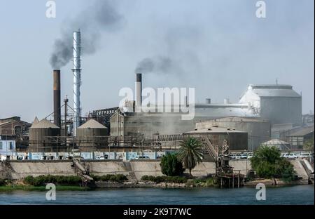 Smoke billows from the chimneys stacks of a sugar refinery which sits on the bank of the River Nile south of Luxor in Egypt. Stock Photo