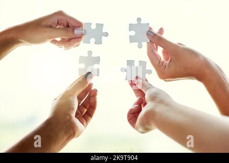 Its a perfect fit. Closeup shot of four unrecognizable people joining puzzle pieces together. Stock Photo