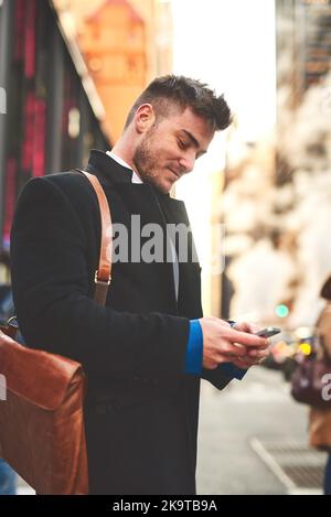 The messages keep coming. a young well dressed man texting on his cellphone while waiting for a taxi to get him to work in the morning. Stock Photo