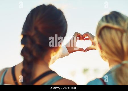 We both really love travelling. Rearview shot of two unrecognizable female friends making a heart shape with their hands in nature. Stock Photo