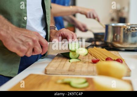 Preparing all the ingredients they need. Closeup shot of an unrecognizable man slicing cucumbers while cooking with his wife at home. Stock Photo