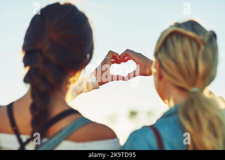 We have a deep love for travelling. Rearview shot of two unrecognizable female friends making a heart shape with their hands in nature. Stock Photo