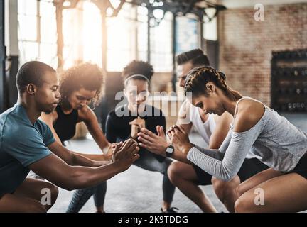 Squatting - The ultimate in lower body exercise. a group of young people doing squats together during their workout in a gym. Stock Photo