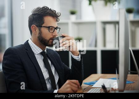 Giving his undivided attention to the task at hand. a young businessman drinking coffee while working in an office. Stock Photo
