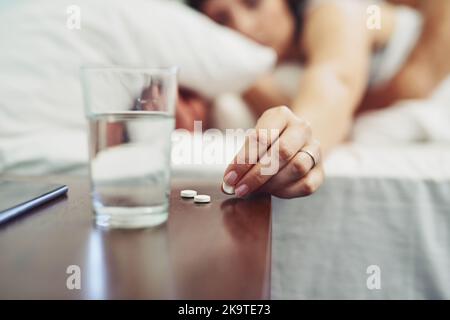 Goodbye headache. an unrecognizable woman lying in bed and taking a pill to drink after waking up sleeping in bed. Stock Photo