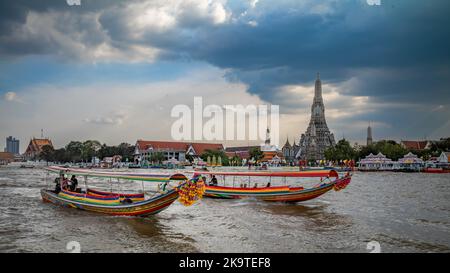 Traditional long tail boats for tourist trips move down the Chao Phraya River opposite Wat Arun, or The Temple of Dawn, in Bangkok, Thailand. Stock Photo