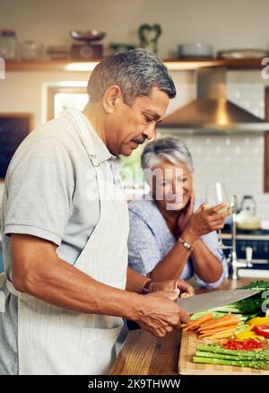 She fell in love with his cooking skills. a happy mature couple cooking a meal together at home. Stock Photo
