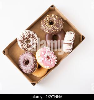 Fresh donuts with different frosted, chocolate, pink glazed and sprinkles on white background with copy space. Assortment of various colourful donuts. Stock Photo