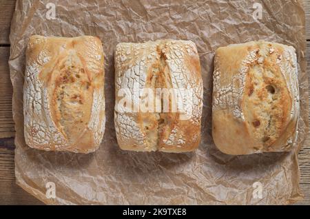 Three loaves of french buns on crumpled paper on wooden table, top view Stock Photo