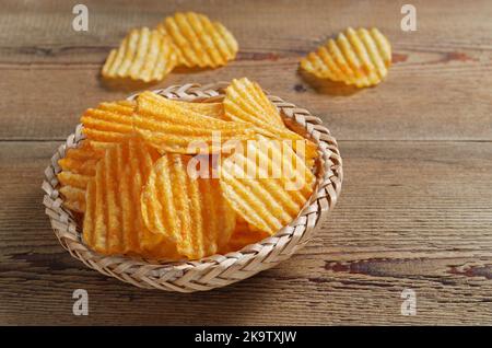 Ribbed potato chips in a wicker bowl on the wooden table close-up Stock Photo