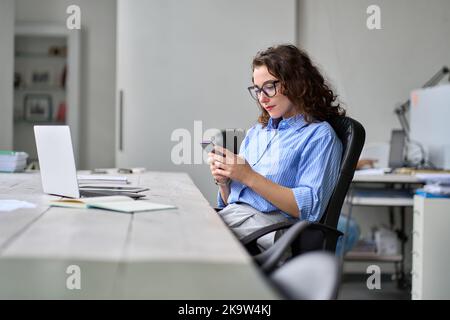 Young business woman using smartphone working in office sitting at desk. Stock Photo