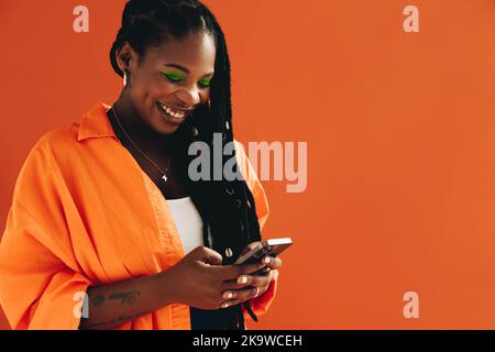 Happy black woman sending a text message on her smartphone in a studio. Cheerful young woman smiling while using her mobile phone. Stylish young woman Stock Photo