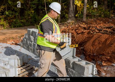 Contractor is constructing a block retaining wall on a construction site while installing newly constructed wall Stock Photo