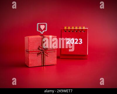 3d love like heart icons floating on small red present gift box with 2023 year of desk calendar on red background. Special gift for Valentine's Day, Stock Photo