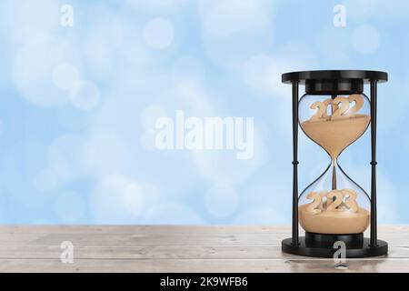 New 2023 Year Concept. Sand Falling in Hourglass Taking the Shape from 2022 to 2023 year on a wooden table. 3d Rendering Stock Photo