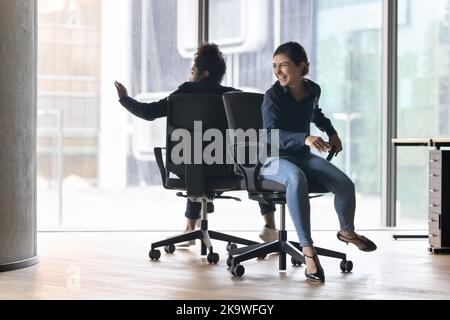 Cheerful Indian office employee riding seated on chairs Stock Photo