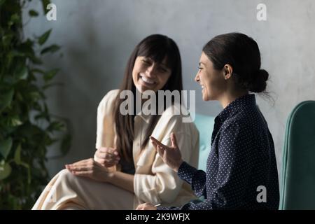 Two cheerful multi ethnic women laughing seated indoor Stock Photo