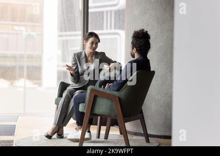 Workmates talking seated on cozy armchairs in modern office lobby Stock Photo