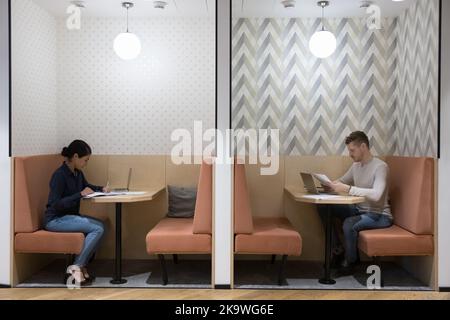 Two young freelancers working seated at tables in modern coworking Stock Photo