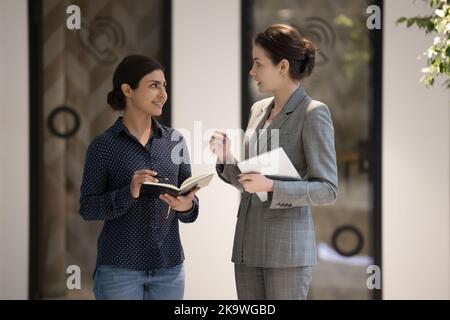 Two multi ethnic businesswomen standing in office hallway and talking Stock Photo