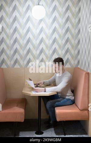 Serious focused businessman typing on laptop holds papers, preparing report Stock Photo