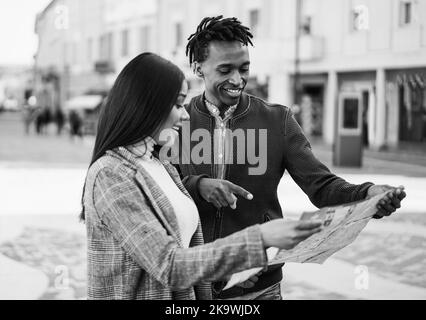 Happy african couple having fun looking city map during travel vacation - Focus on man face - Black and white editing Stock Photo