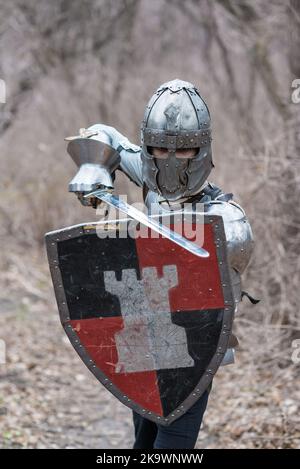 Noble warrior. Portrait of one medeival warrior or knight in armor and helmet with shield and sword posing isolated over dark background. Stock Photo