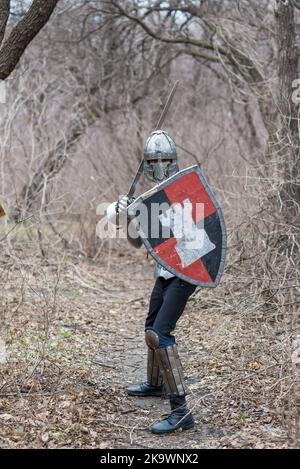 Noble warrior. Portrait of one medeival warrior or knight in armor and helmet with shield and sword posing isolated over dark background. Stock Photo