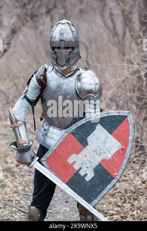 Noble warrior. Portrait of one medeival warrior or knight in armor and helmet with shield and sword posing isolated over dark background. Stock Photo