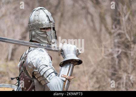 Noble warrior. Portrait of one medeival warrior or knight in armor and helmet with shield and sword posing isolated over dark background. Stock Photo