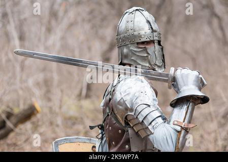 Noble warrior. Portrait of one medeival warrior or knight in armor and helmet with shield and sword posing isolated over dark background. Stock Photo