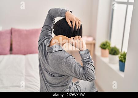 Young chinese woman combing hair sitting on bed at bedroom Stock Photo