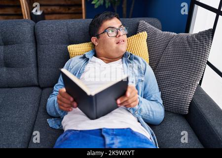Down syndrome man reading book lying on sofa at home Stock Photo