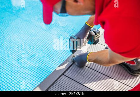 Poolside Composite Deck Building by Professional Worker. Modern Swimming Pool Surrounding. Using Cordless Drill Driver. Stock Photo