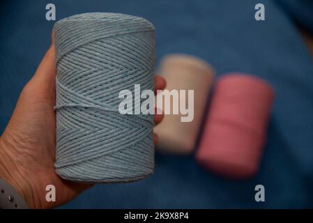 Coil of blue macrame thread in the hand on a blue backgraound Stock Photo