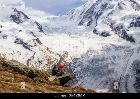 Mother and daughter sitting on a stone and looking at panorama of the Pennine Alps with famous Gorner Glacier and impressive snow capped Monte Rosa Ma Stock Photo